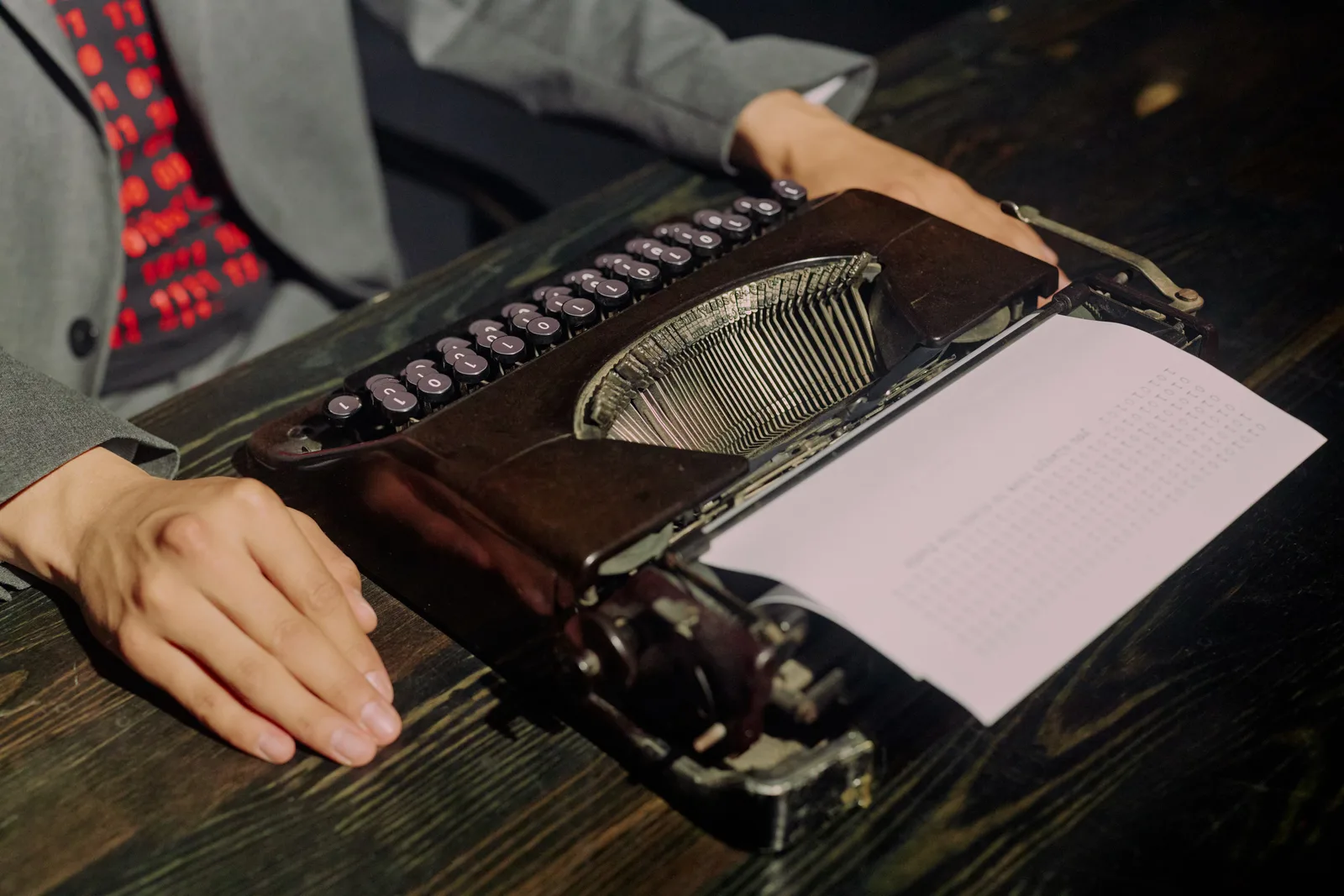 A person uses a vintage typewriter to type on paper in a retro office setting.