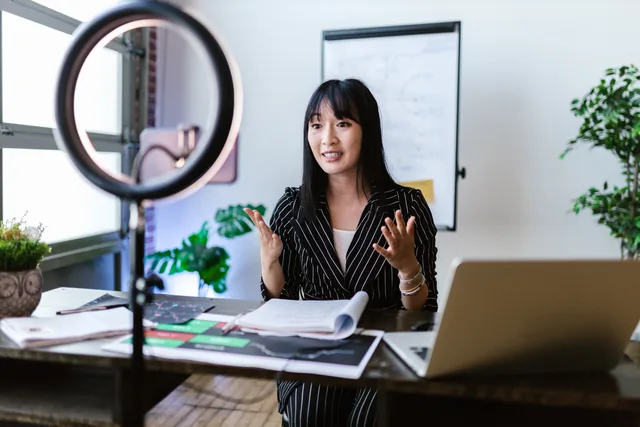 Female vlogger recording a professional video with a ring light setup, discussing finance topics. Weryfikacja jakości odbiorców